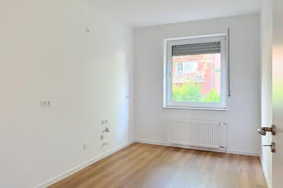 Frisch renovierter Raum in Mietwohnung, mit Fenster, weiße Wände und neuer Laminatboden in hellem Braun